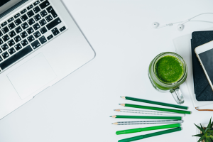 laptop on white table with green pencils and a green smoothie a glass jar