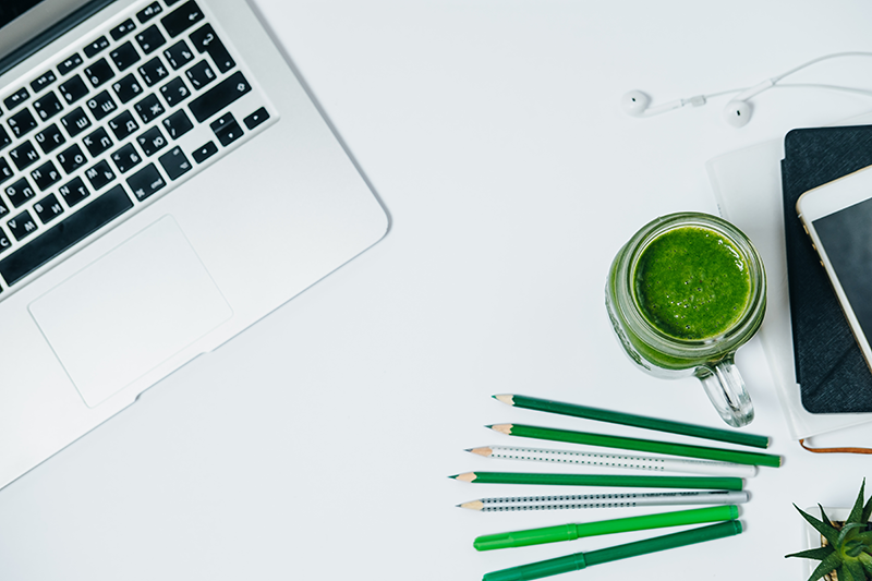 laptop on white table with green pencils and a green smoothie a glass jar