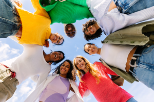 diverse group of people hugging in a circle and looking down at the camera